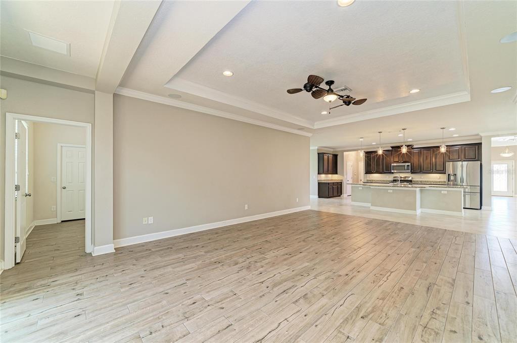 An open-concept living area with light wood-look tile flooring leads into a kitchen with dark cabinetry — 12821 BALSAM TERRACE, BRADENTON, FL