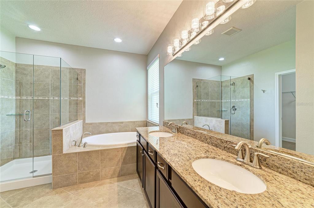 A bathroom with a double vanity, granite countertops, a soaking tub, and a glass-enclosed shower — 12821 BALSAM TERRACE, BRADENTON, FL