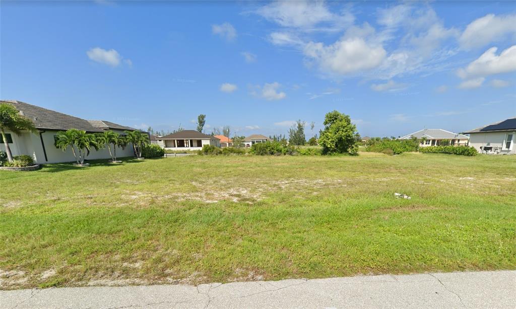 A vacant, grassy residential lot sits between two single-story houses under a blue sky — 718 NW 38TH PLACE, CAPE CORAL, FL