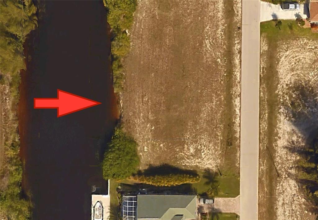 This aerial view shows a vacant waterfront lot situated between a canal and a paved road — 718 NW 38TH PLACE, CAPE CORAL, FL