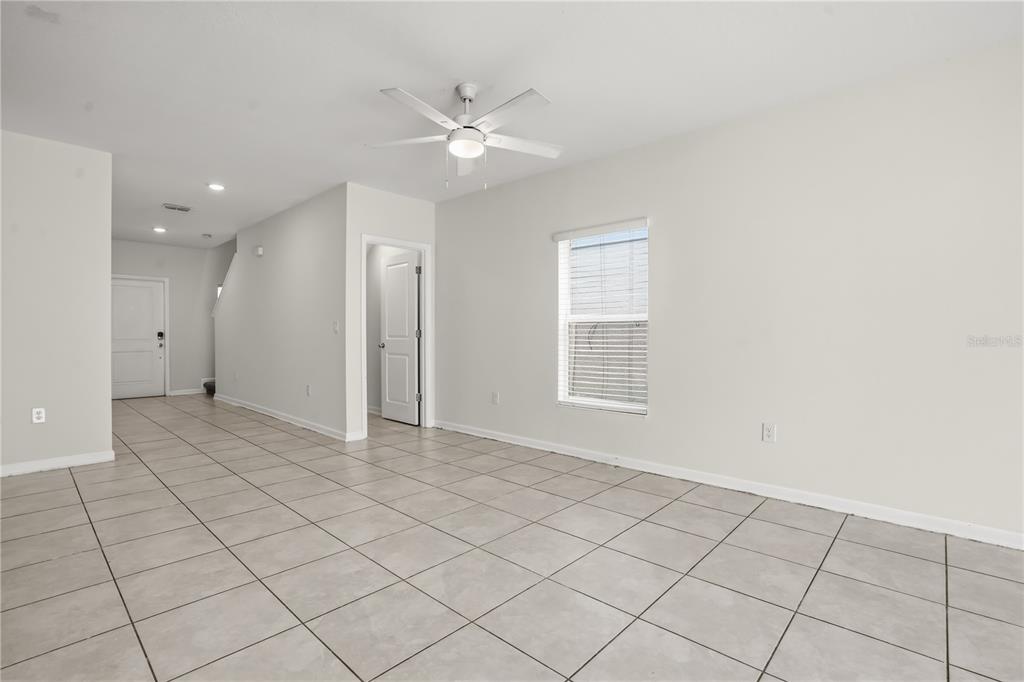 A bright, empty living room features light-colored tile flooring, white walls, and a ceiling fan — 1721 WHITE WATER COURT, DAVENPORT, FL