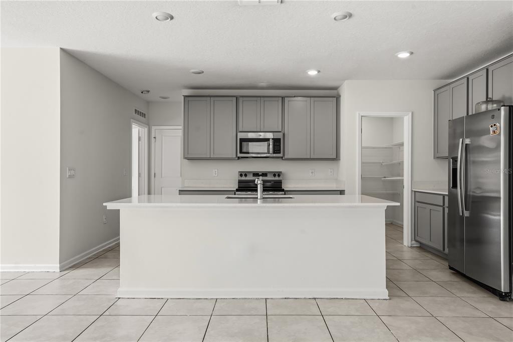 A kitchen with a white island, gray cabinets, stainless steel appliances, and tile flooring — 1721 WHITE WATER COURT, DAVENPORT, FL