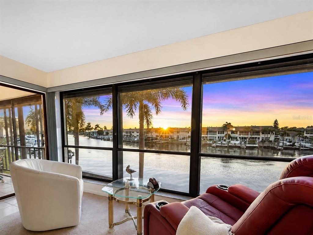 A sunroom features a glass-topped table, two armchairs, and large windows overlooking a waterfront canal — 4218 SE 20TH PLACE UNIT D5, CAPE CORAL, FL