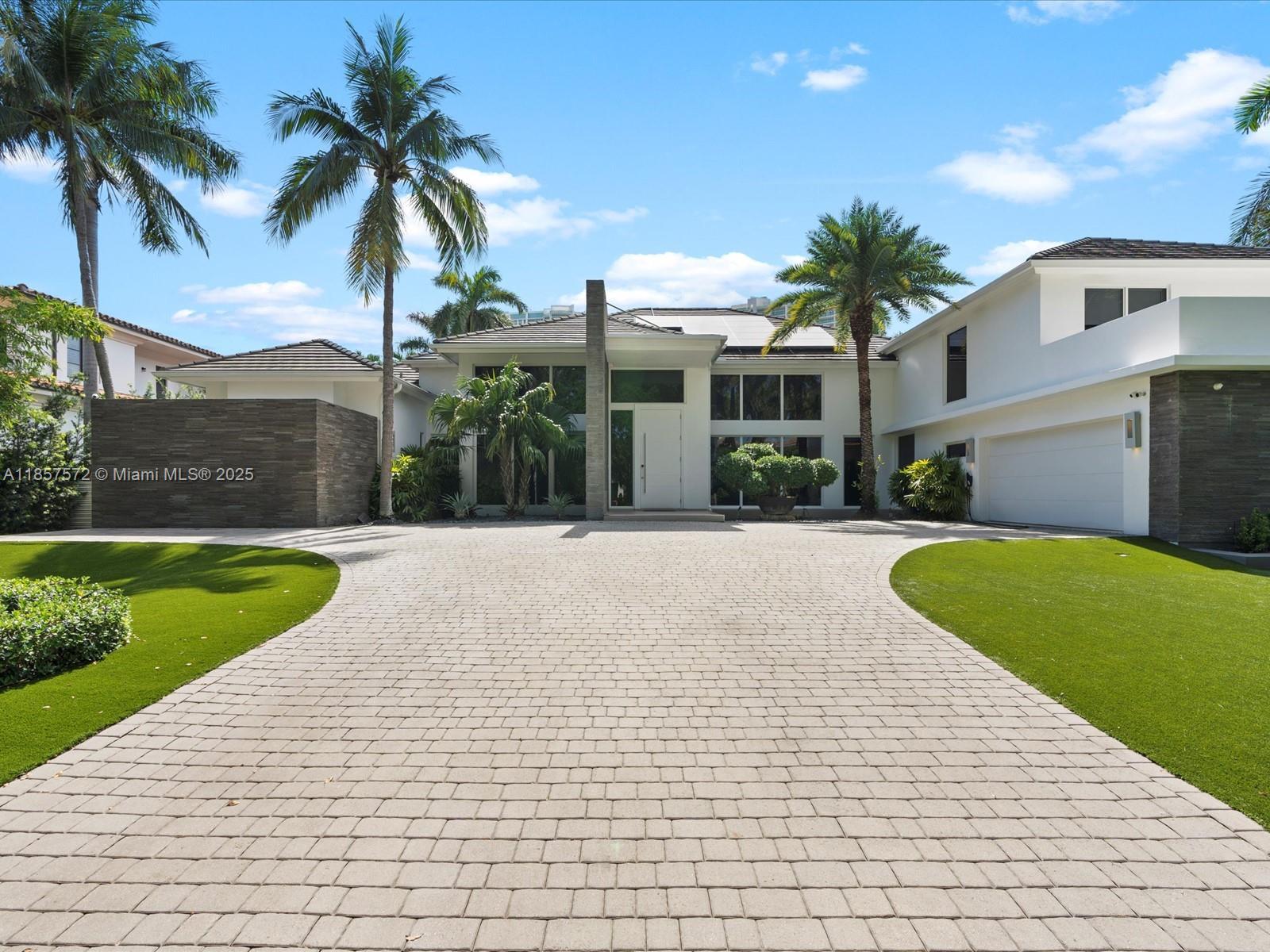 A modern house with a paved driveway, manicured lawn, and palm trees under a blue sky — 224 S ISLAND, Golden Beach FL 33160, GOLDEN BEACH, FL