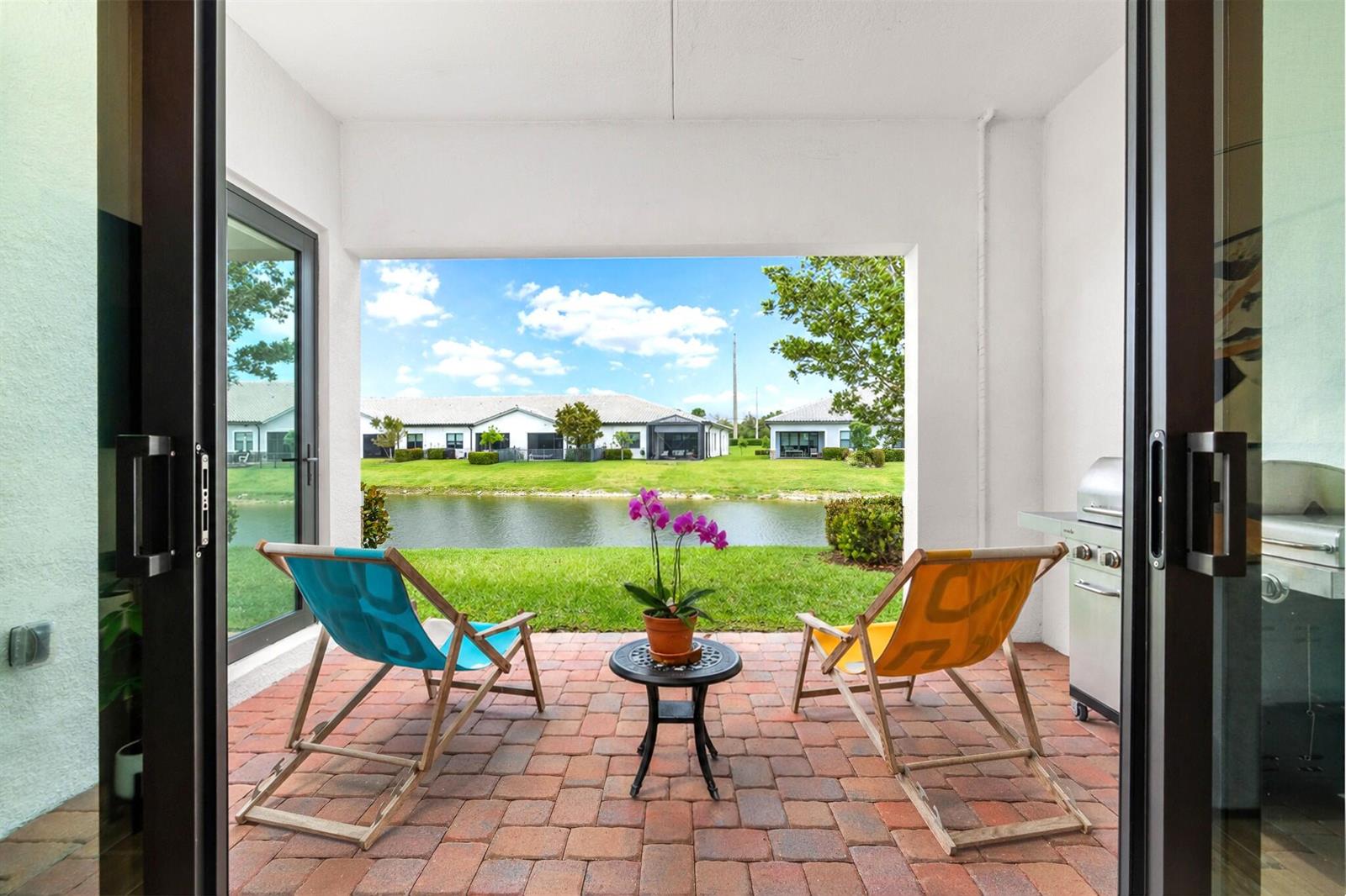A patio with two lounge chairs, a small table, and a grill overlooks a pond — 7621 S Blue Spring Drive, Parkland FL 33067, PARKLAND, FL