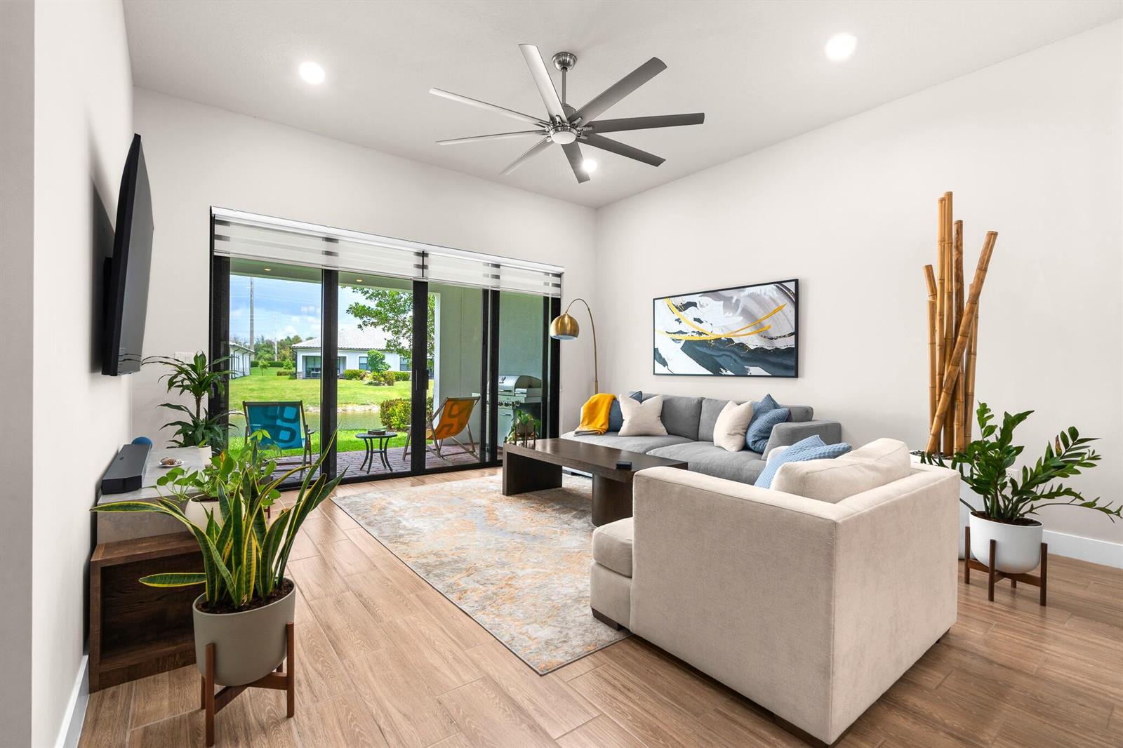 A living room with a gray sectional, beige armchair, ceiling fan, and sliding glass doors — 7621 S Blue Spring Drive, Parkland FL 33067, PARKLAND, FL