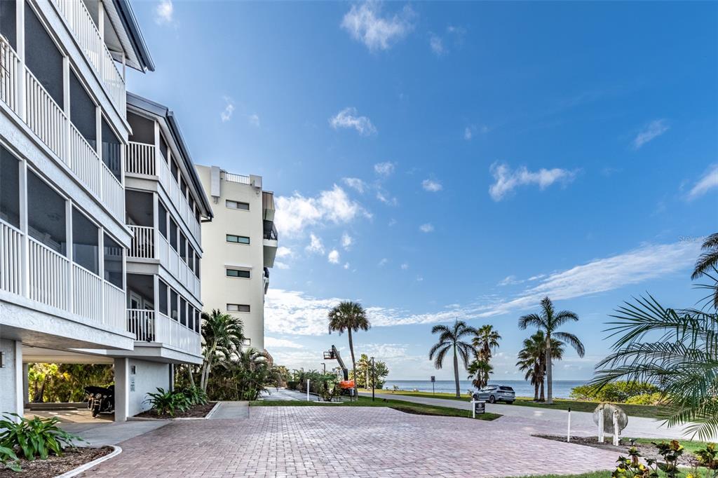 A multi-story apartment building stands next to a paved driveway overlooking the ocean and palms — 1477 PARK BEACH CIRCLE UNIT 11, PUNTA GORDA, FL