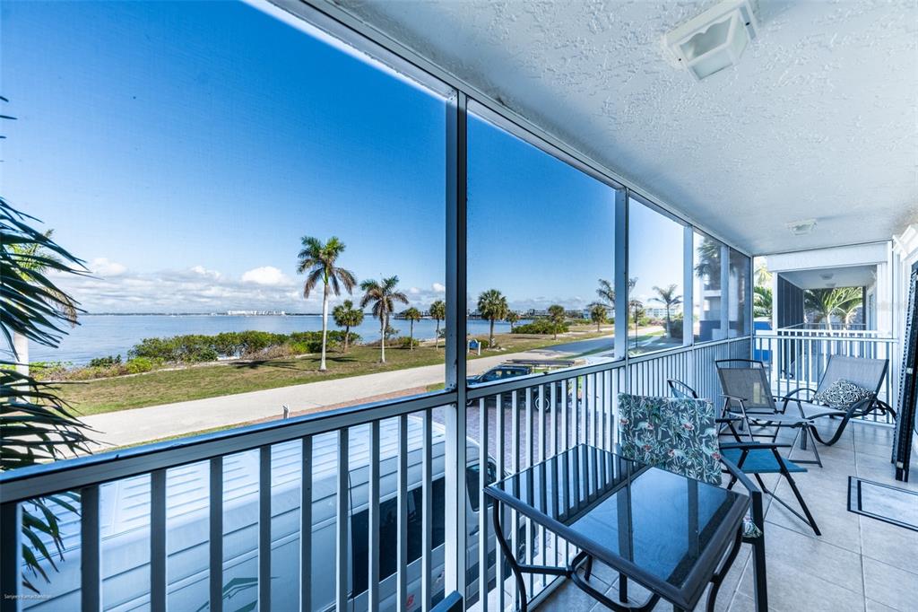 A screened-in balcony with outdoor furniture overlooks a coastal landscape with palm trees and water — 1477 PARK BEACH CIRCLE UNIT 11, PUNTA GORDA, FL