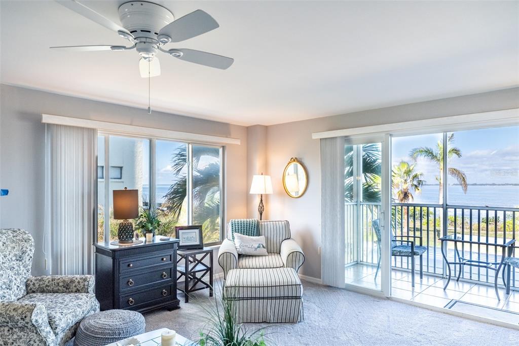 A living room features a ceiling fan, striped armchair, dark dresser, and sliding glass balcony doors — 1477 PARK BEACH CIRCLE UNIT 11, PUNTA GORDA, FL