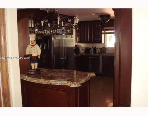A kitchen features dark wood cabinets, granite countertops, and a decorative chef statue on the island — 12425 SW 43rd St, Miami FL 33175, MIAMI, FL
