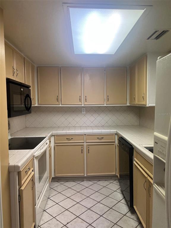 A kitchen features tan cabinets, white tiled countertops, a white floor, and black appliances — 200 MAITLAND AVENUE UNIT 1, ALTAMONTE SPRINGS, FL