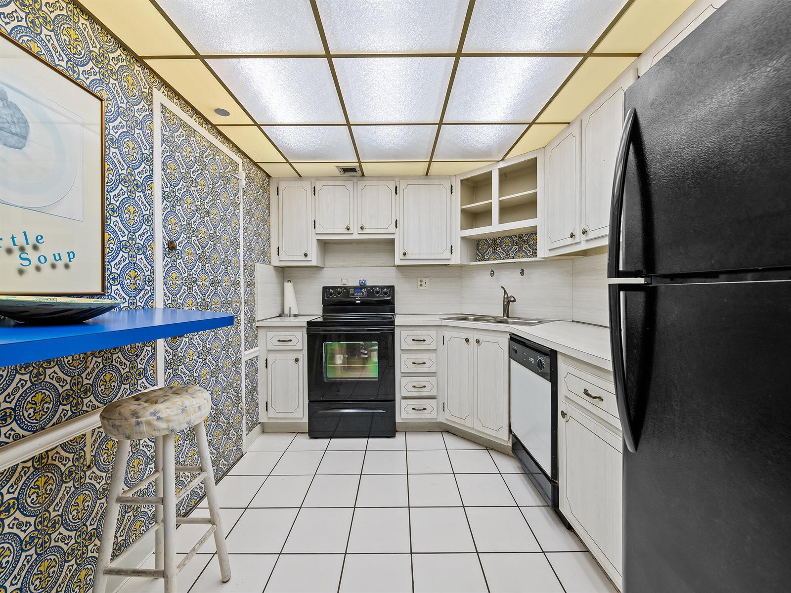 A kitchen features white cabinets, black appliances, patterned wallpaper, and a grid-style drop ceiling — 2500 E Las Olas Boulevard # 404, Fort Lauderdale FL 33301, FORT LAUDERDALE, FL