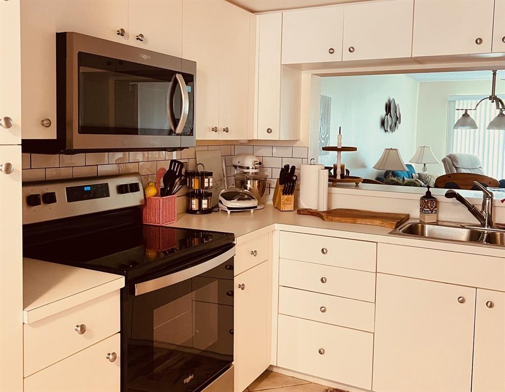 A kitchen with white cabinets, stainless steel appliances, and a pass-through window to the living area — 9330 CLUBSIDE CIRCLE UNIT 3209, SARASOTA, FL