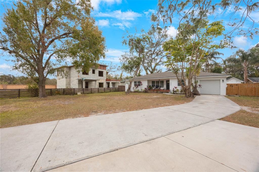 A white single-story house with a concrete driveway sits next to an unfinished block structure — 2504 W FLETCHER AVENUE, TAMPA, FL