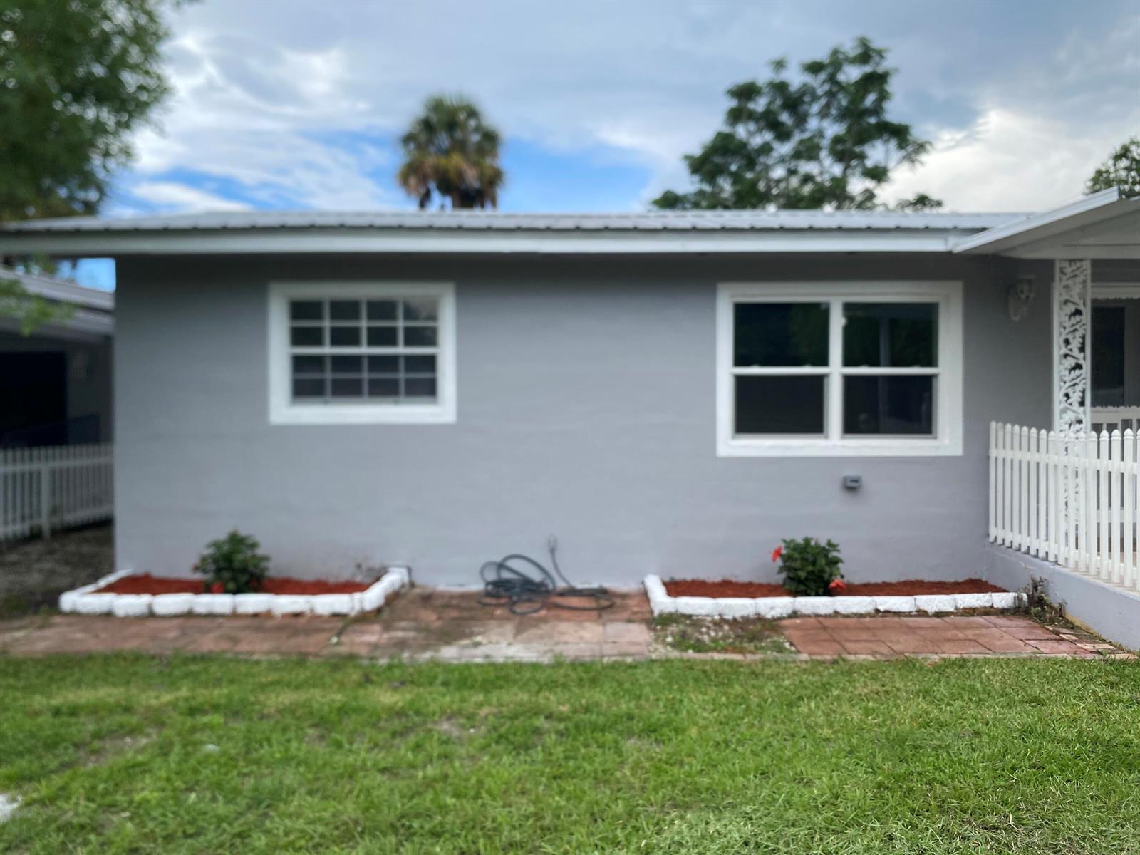 The exterior of a gray house features two windows, two small garden beds, and landscaping — 1788 SW 8th Street, Okeechobee FL 34974, OKEECHOBEE, FL