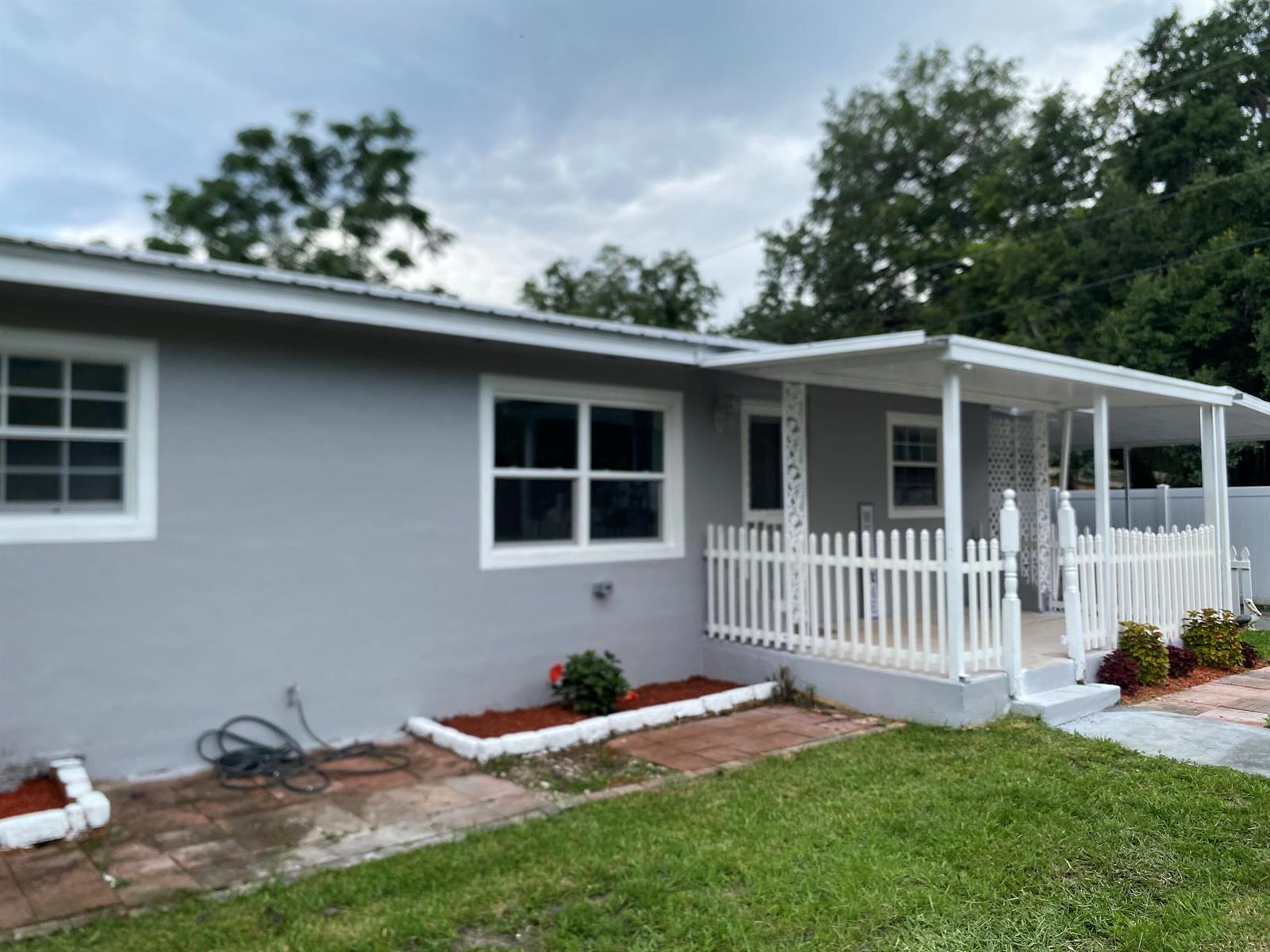 A gray house features a white picket fence, a covered porch, and red-mulched garden beds — 1788 SW 8th Street, Okeechobee FL 34974, OKEECHOBEE, FL