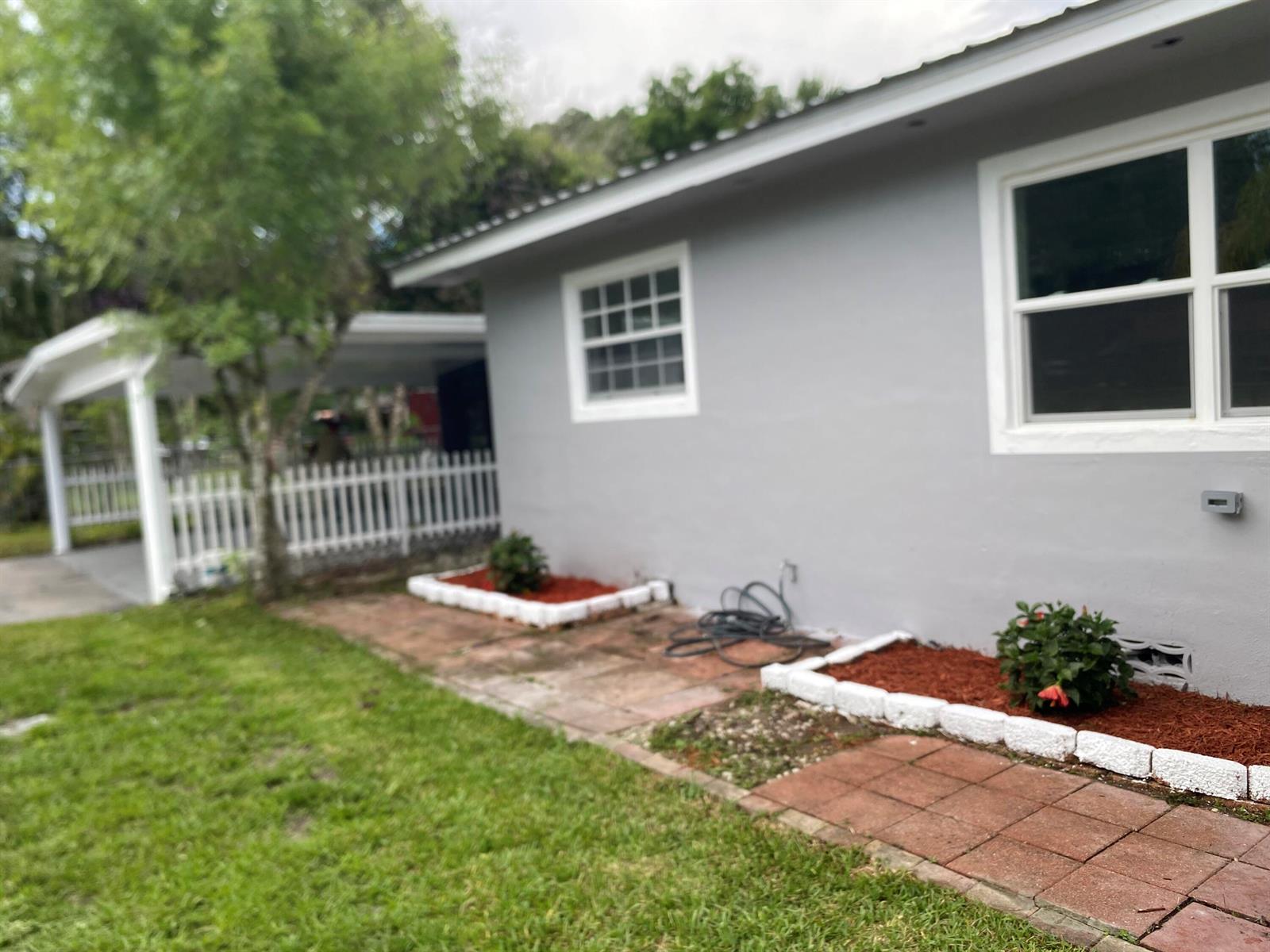 A gray house exterior features a brick walkway, white-bordered garden beds, and a white fence — 1788 SW 8th Street, Okeechobee FL 34974, OKEECHOBEE, FL
