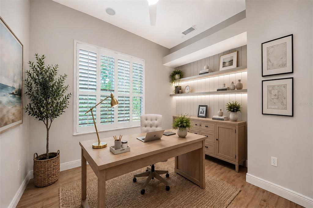 A home office features a wooden desk, built-in shelving with lighting, and plantation shutters — 3921 MARAVIC PLACE, SARASOTA, FL