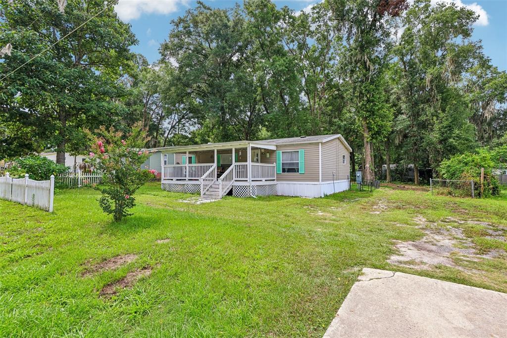 A single-story manufactured home with a front porch sits on a grassy, wooded lot — 4884 SE 146TH LANE, SUMMERFIELD, FL