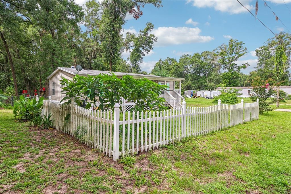 A single-story manufactured home sits behind a white picket fence in a grassy yard — 4884 SE 146TH LANE, SUMMERFIELD, FL