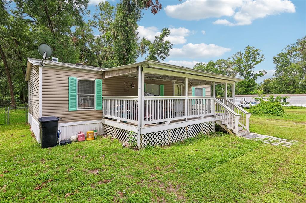 A tan mobile home features a large covered wooden deck with white railings and lattice — 4884 SE 146TH LANE, SUMMERFIELD, FL
