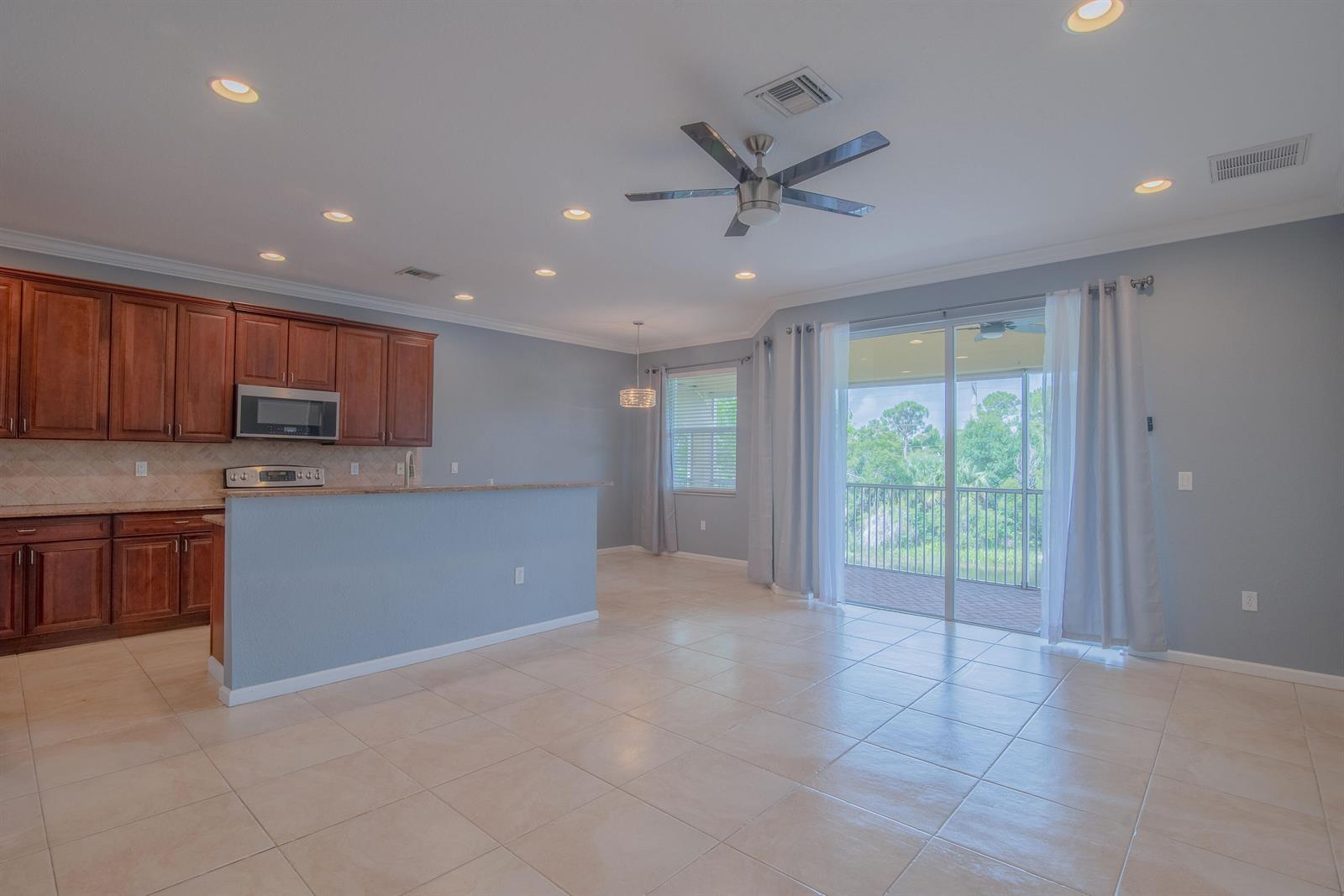 An open-concept kitchen and living area features wood cabinets, tile flooring, and a sliding door — 7522 SW Herrington Lane, Stuart FL 34997, STUART, FL