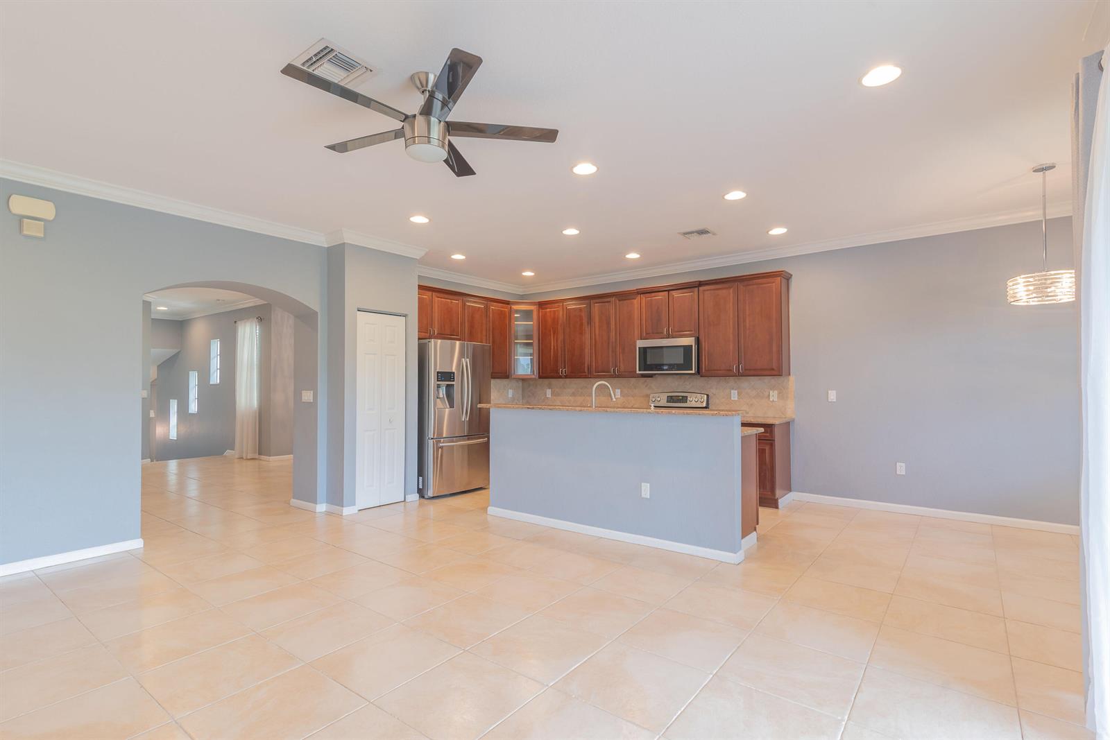A kitchen with wood cabinets, stainless steel appliances, and an island overlooks a tiled room — 7522 SW Herrington Lane, Stuart FL 34997, STUART, FL
