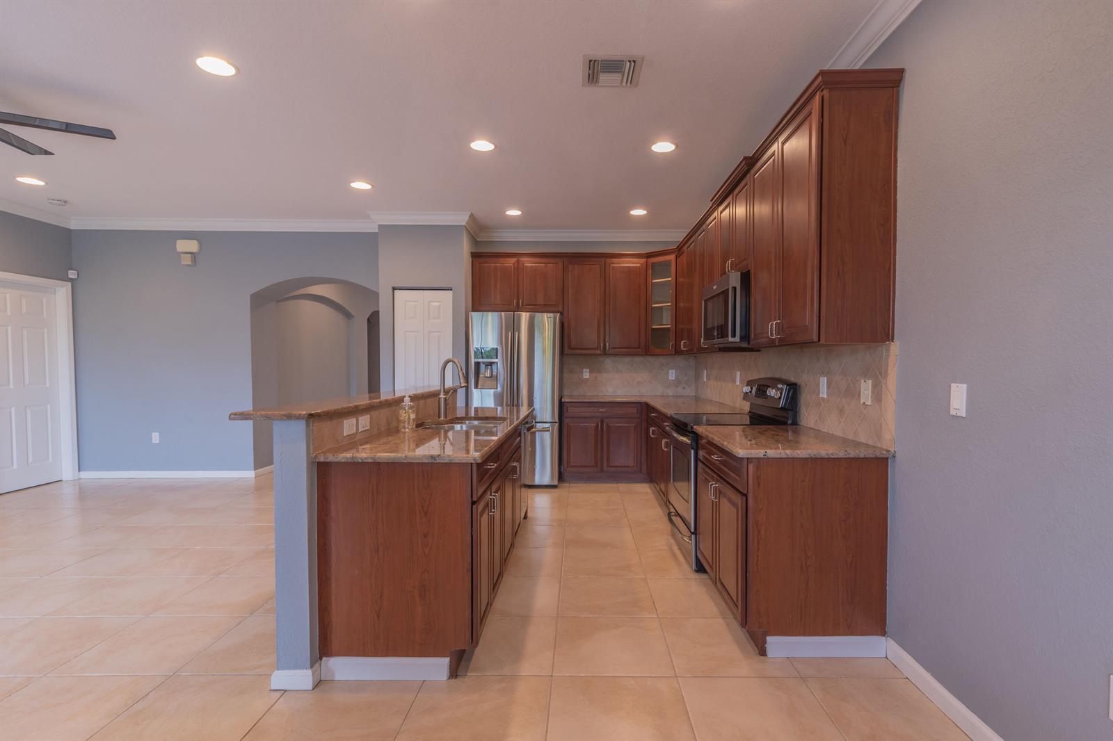 A kitchen with dark wood cabinets, granite countertops, stainless steel appliances, and tile flooring — 7522 SW Herrington Lane, Stuart FL 34997, STUART, FL