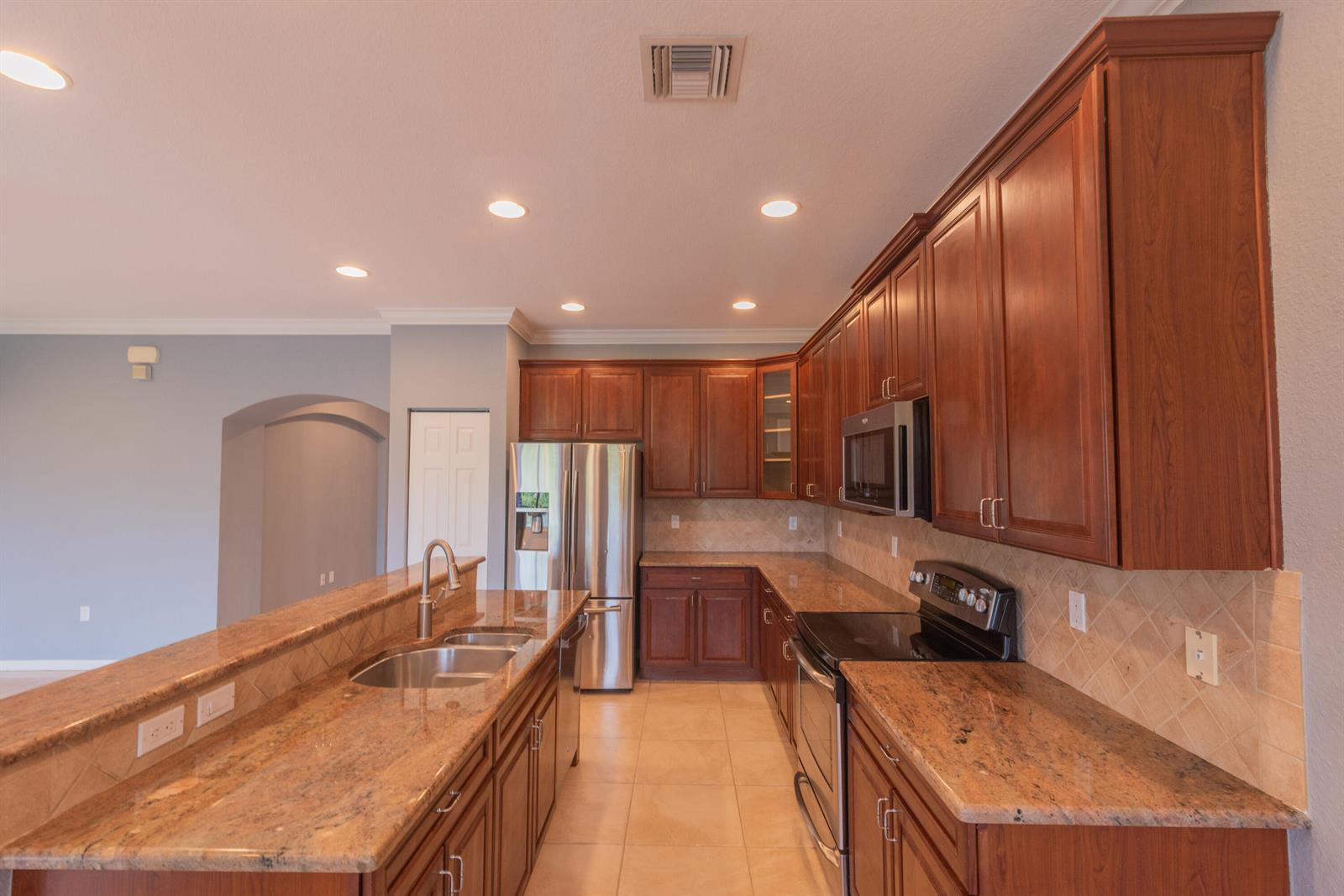A kitchen features wood cabinets, granite countertops, stainless steel appliances, and tile flooring — 7522 SW Herrington Lane, Stuart FL 34997, STUART, FL