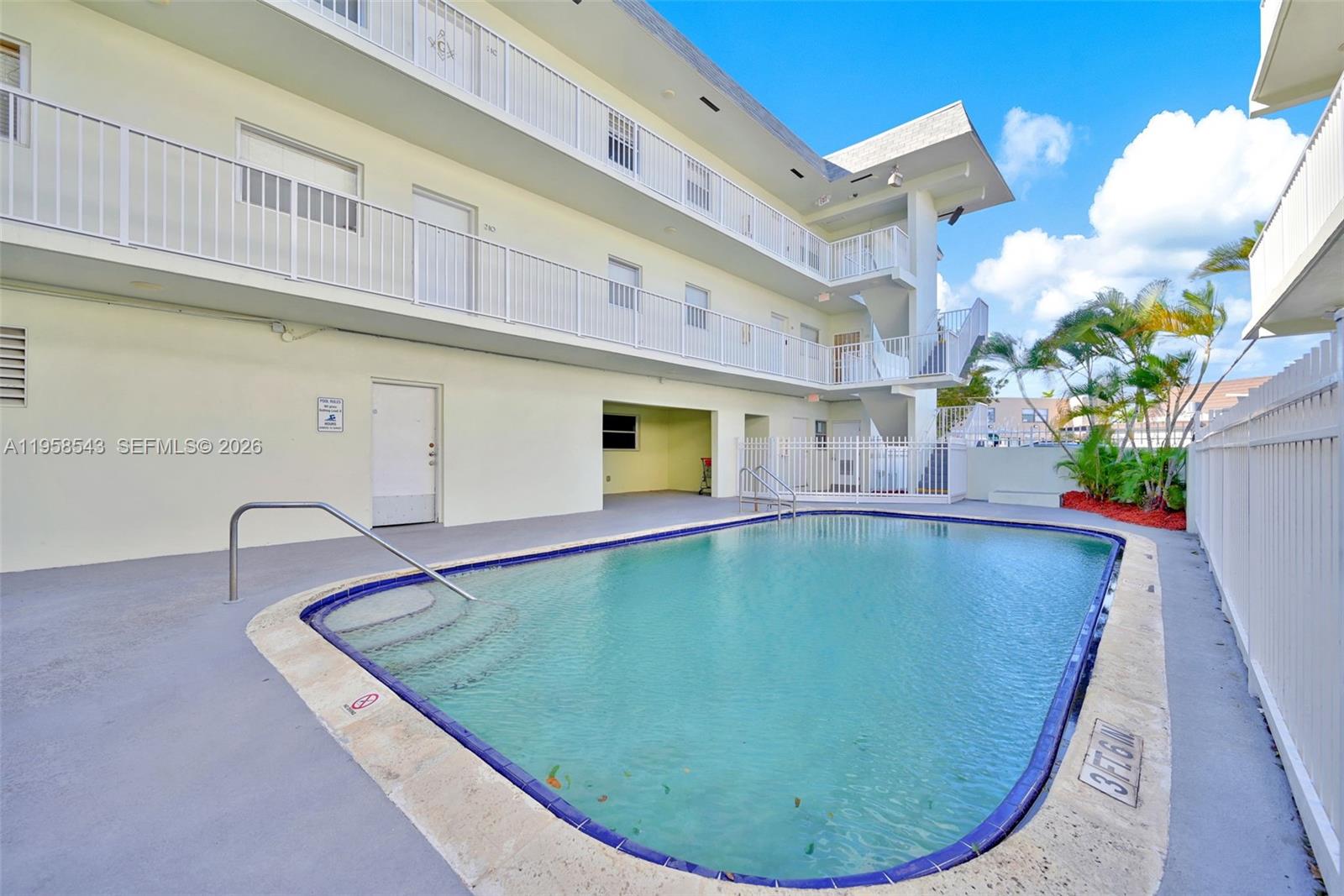 A swimming pool sits in front of a multi-story apartment building with exterior walkways — 12890 NE 8th Ave # 208, North Miami FL 33161, NORTH MIAMI, FL