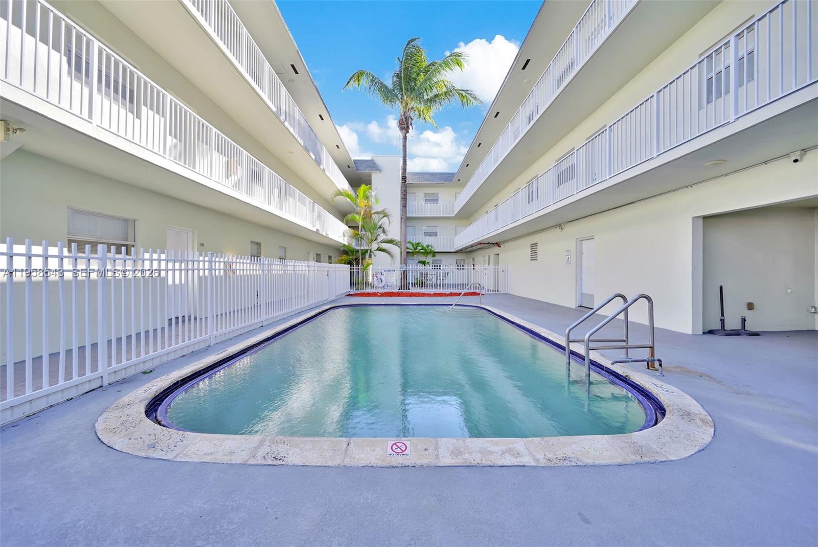 An outdoor swimming pool is situated between two multi-story apartment buildings with white railings — 12890 NE 8th Ave # 208, North Miami FL 33161, NORTH MIAMI, FL