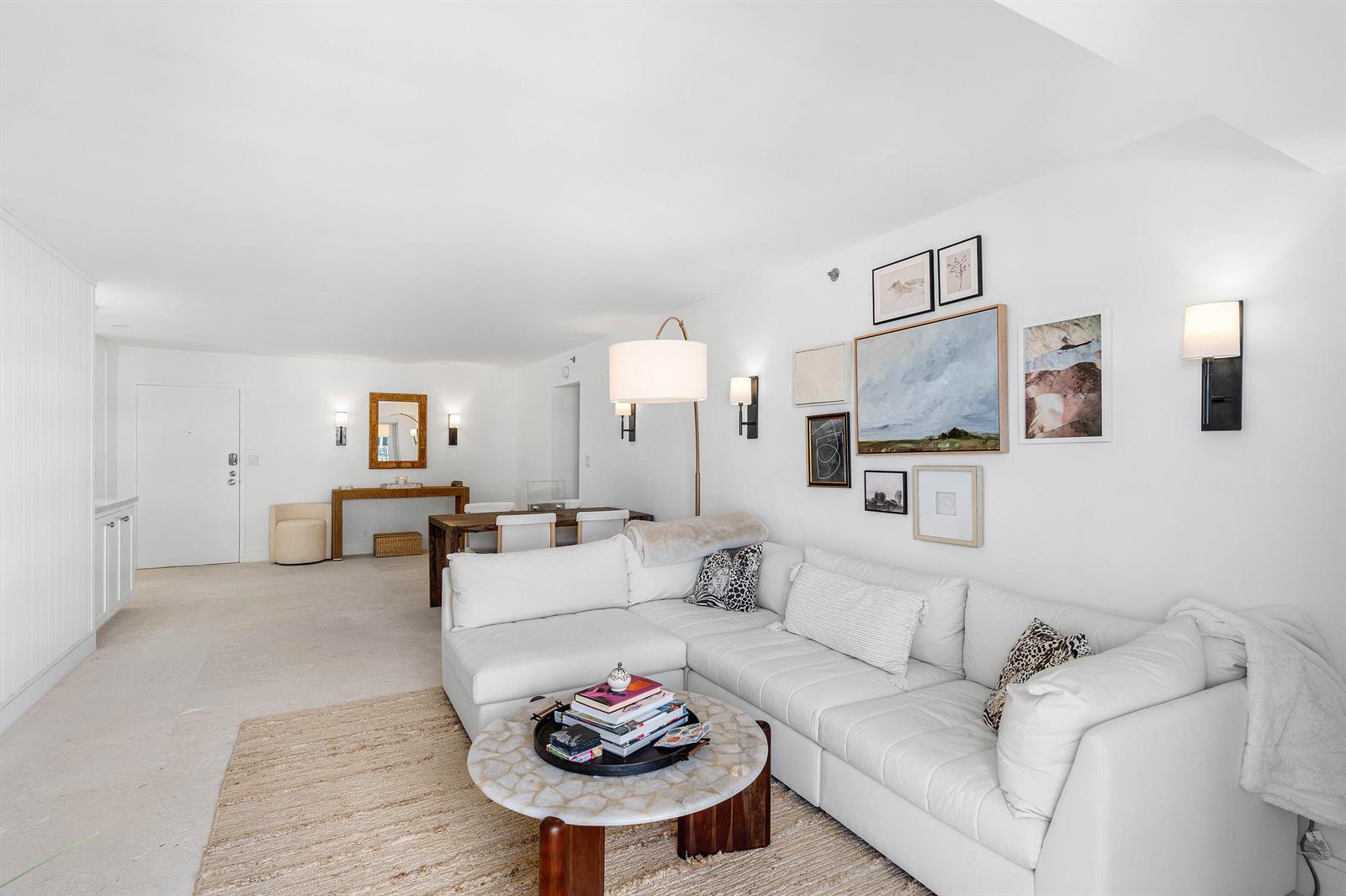 A bright living room features a white sectional sofa, a round coffee table, and gallery wall — 3301 S Ocean Boulevard # 810, Highland Beach FL 33487, HIGHLAND BEACH, FL