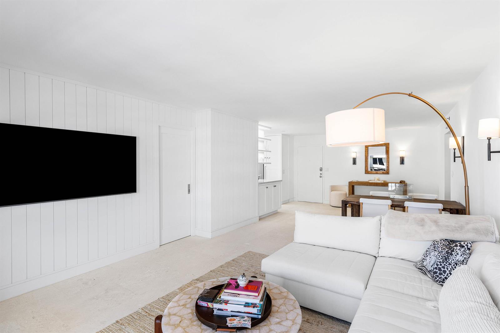 A bright living room features white paneled walls, a large television, and a white sectional — 3301 S Ocean Boulevard # 810, Highland Beach FL 33487, HIGHLAND BEACH, FL