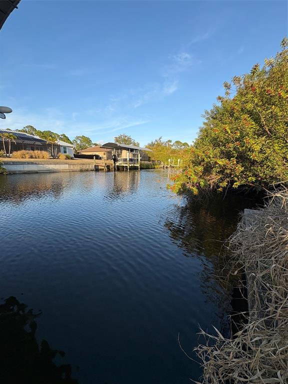 A canal view featuring a boat lift, residential homes, and lush vegetation along the bank — 13333 PALAU CIRCLE, PORT CHARLOTTE, FL