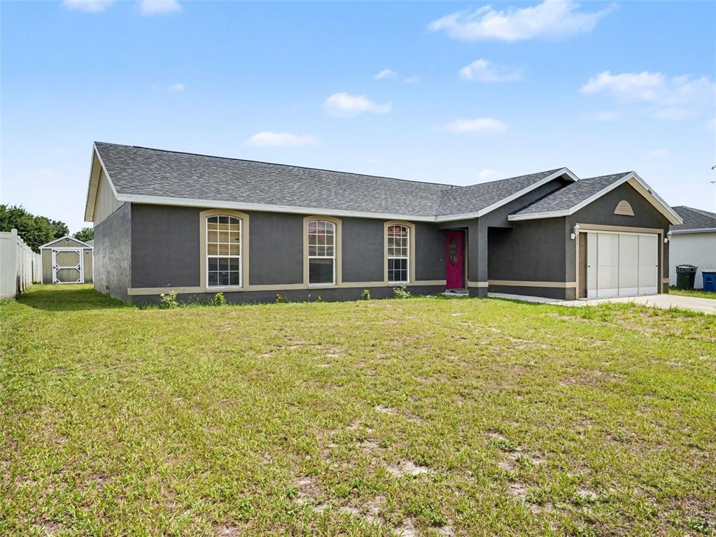 A single-story house with dark gray stucco siding, a pink front door, and an attached garage — 1335 LAUREL GLEN DR, BARTOW, FL