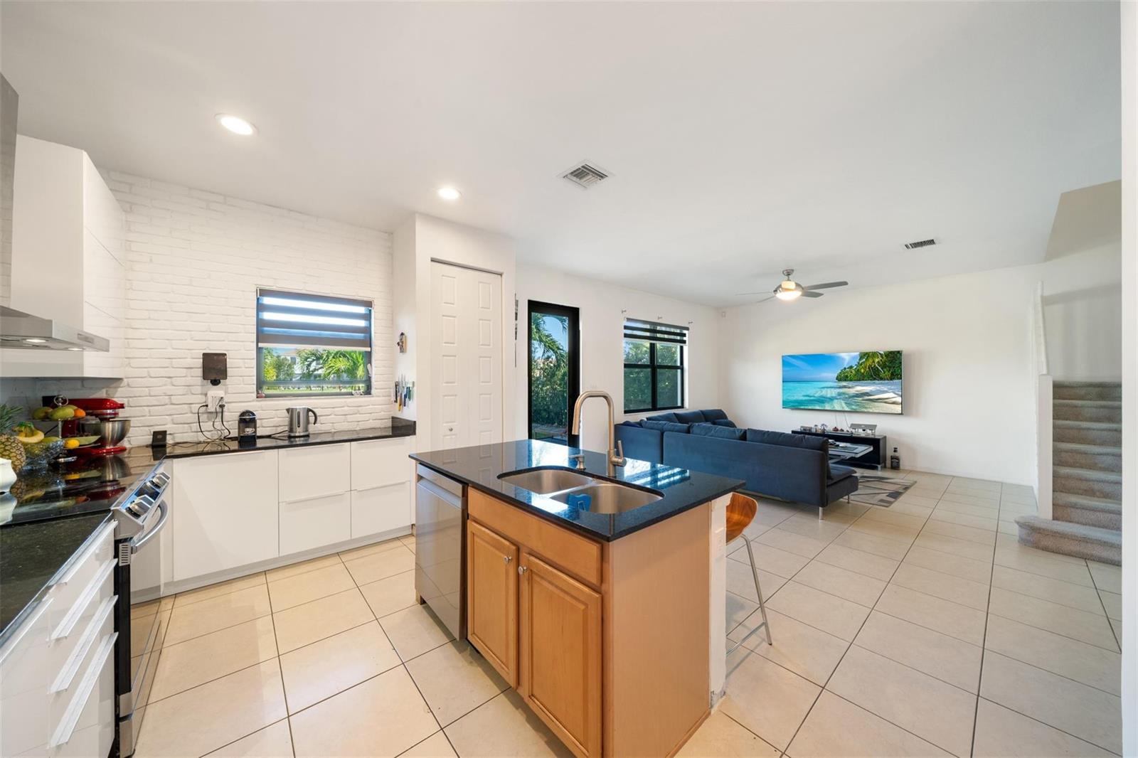 A kitchen with white cabinets and a brick wall opens into a living room area — 631 NE 191st Terrace, Miami FL 33179, MIAMI, FL
