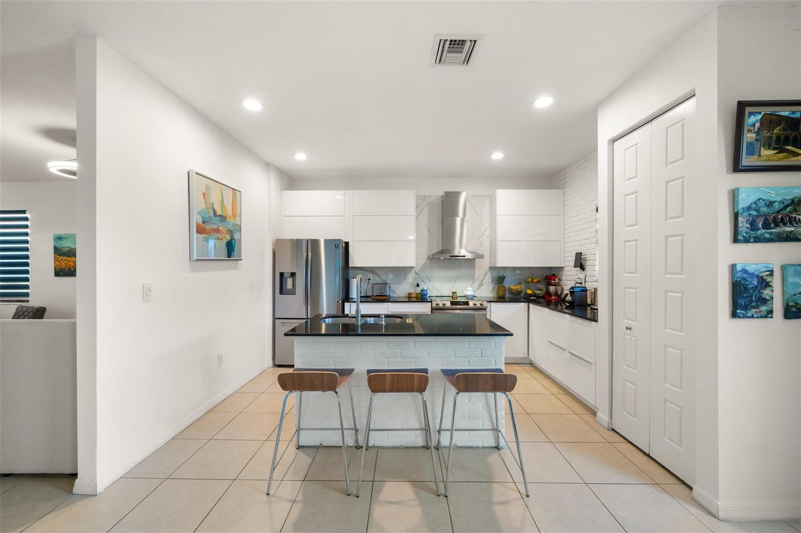 A modern kitchen features white cabinets, a black island, stainless steel appliances, and tile flooring — 631 NE 191st Terrace, Miami FL 33179, MIAMI, FL