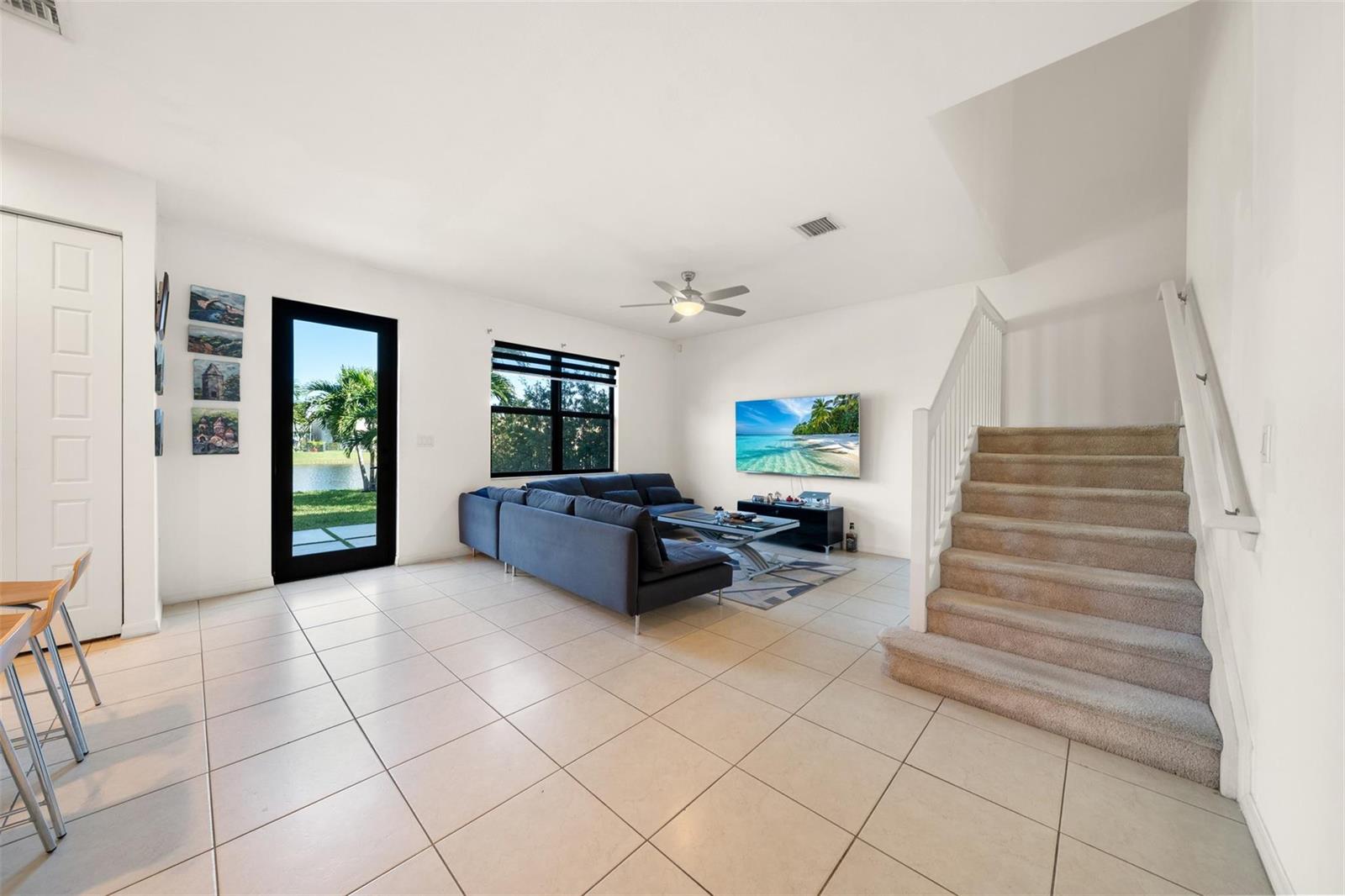 A living room with tile flooring, a gray sectional sofa, a television, and carpeted stairs — 631 NE 191st Terrace, Miami FL 33179, MIAMI, FL