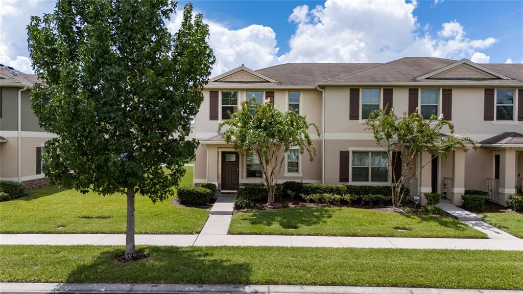 A two-story townhouse with a beige stucco exterior, brown shutters, and a front lawn — 1854 KATZ CROSSING DRIVE, KISSIMMEE, FL