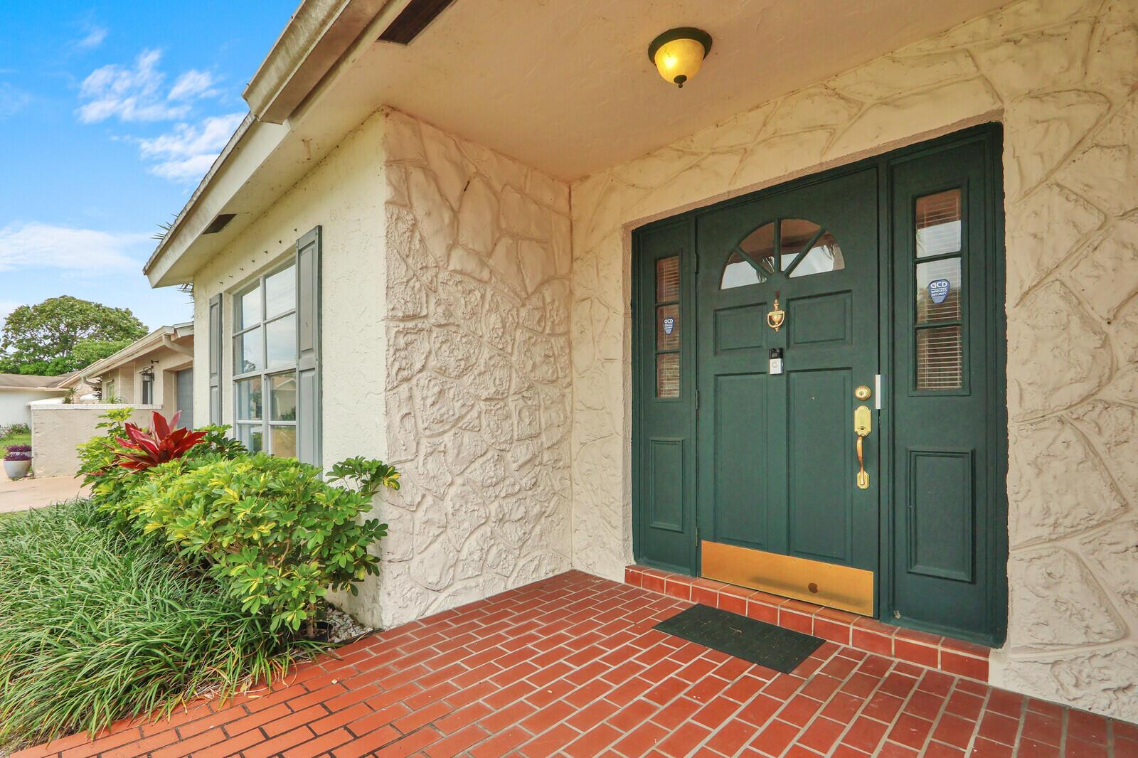 A front entrance with a dark green door, brick porch, and stone-textured exterior wall — 7156 Pine Bluff Drive, Lake Worth FL 33467, LAKE WORTH, FL