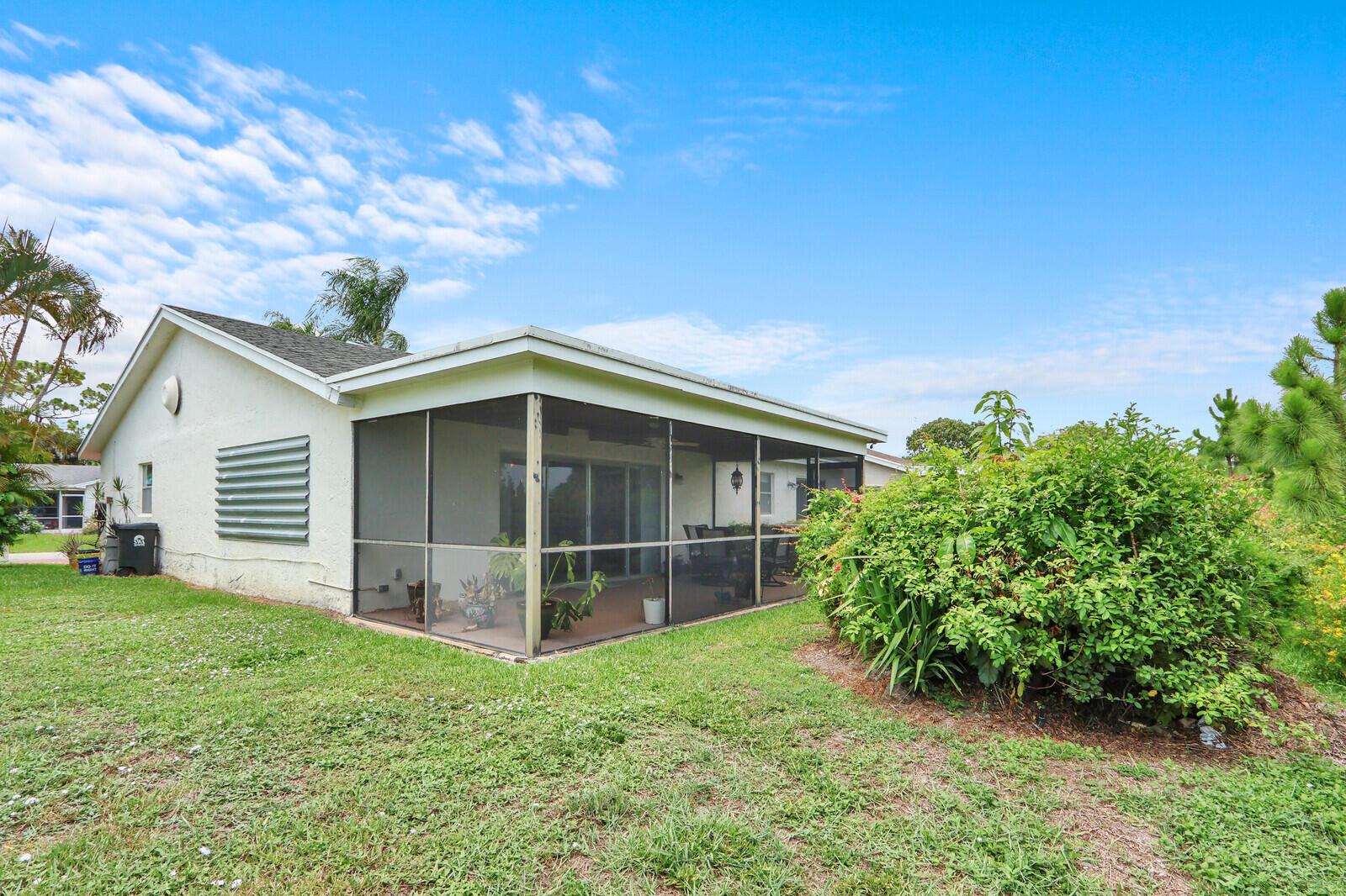 The exterior of a house features a screened-in porch and a large green bush — 7156 Pine Bluff Drive, Lake Worth FL 33467, LAKE WORTH, FL