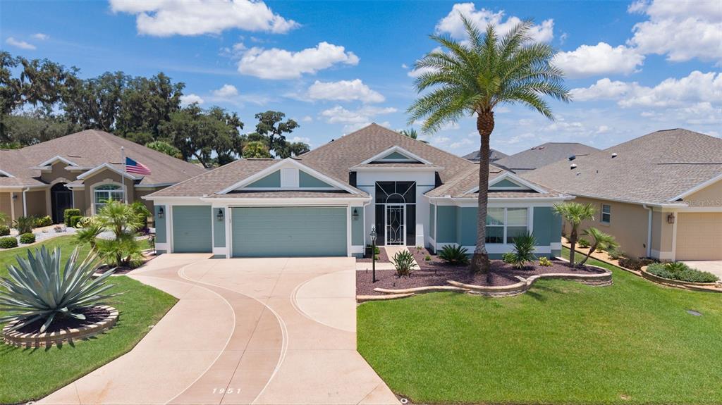 A single-story suburban house with a three-car garage, palm tree, and landscaped front yard — 1951 GATEHOUSE TERRACE, THE VILLAGES, FL