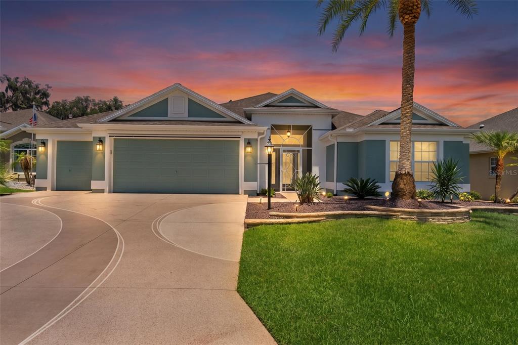 A single-story house with a blue exterior, a three-car garage, and a curved concrete driveway — 1951 GATEHOUSE TERRACE, THE VILLAGES, FL