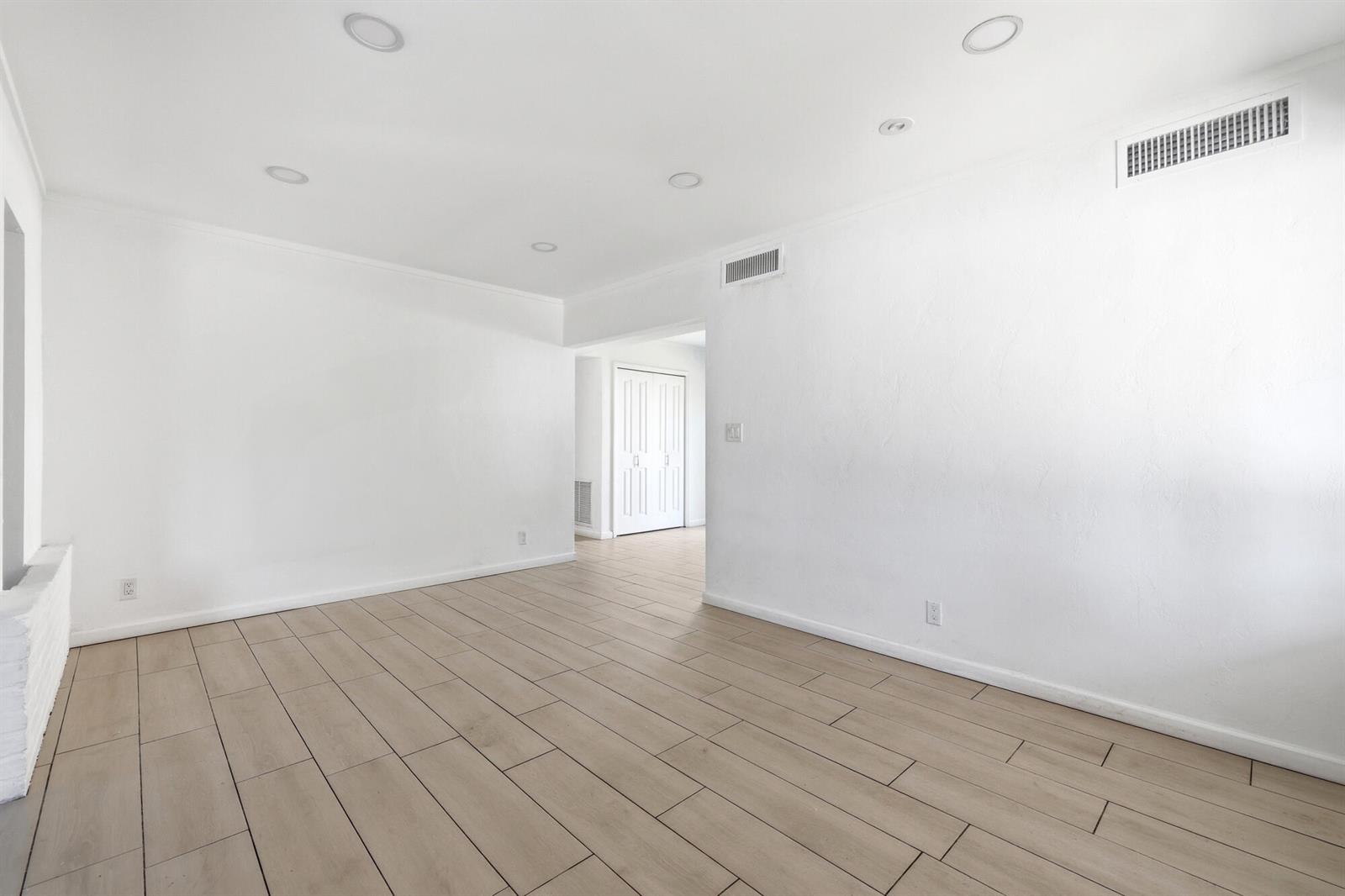 A bright, empty room features light wood-look tile flooring, white walls, and recessed ceiling lights — 1225 15th Avenue N, FL 33460, FL