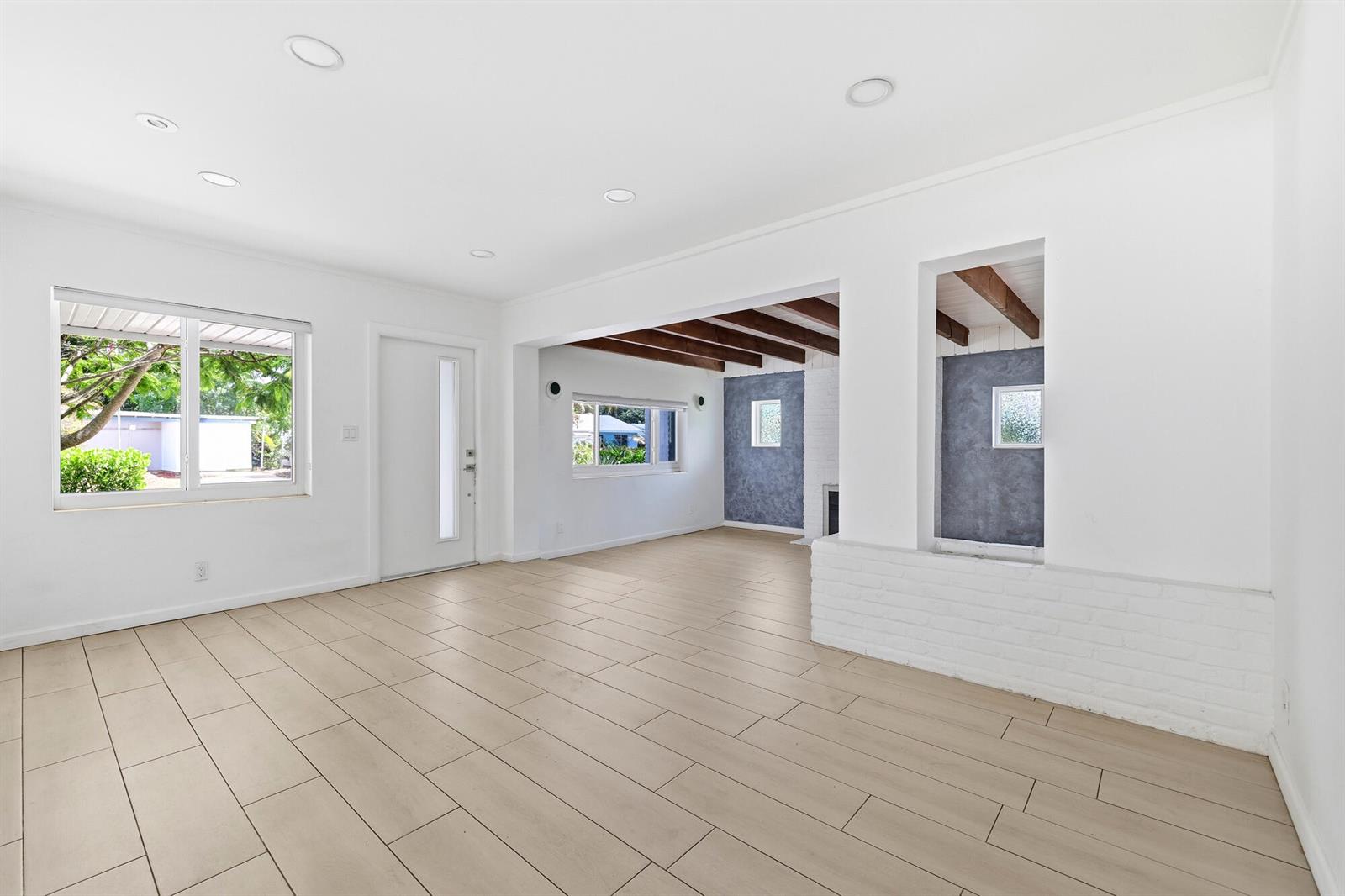 A bright living room features light-colored tile flooring, white walls, and exposed wooden ceiling beams — 1225 15th Avenue N, FL 33460, FL