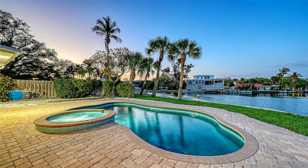 A swimming pool and spa sit on a brick patio overlooking a canal and house — 339 TREASURE BOAT WAY, SARASOTA, FL