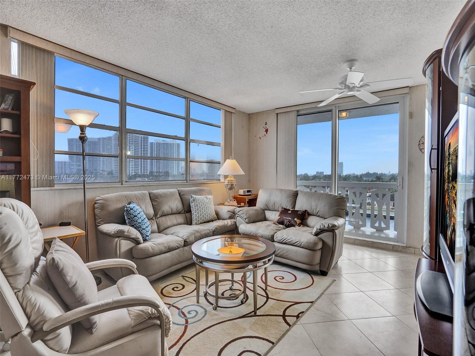 A living room with light tile floors, a sectional sofa, and floor-to-ceiling windows overlooking buildings — 3113 S Ocean Dr # 710, Hallandale Beach FL 33009, HALLANDALE BEACH, FL