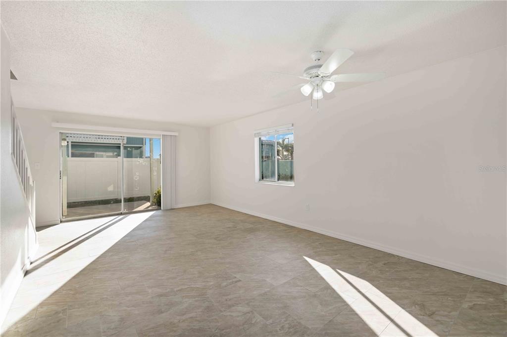 An empty living room features light-colored tile flooring, white walls, a ceiling fan, and sliding doors — 3569 BEE RIDGE, SARASOTA, FL