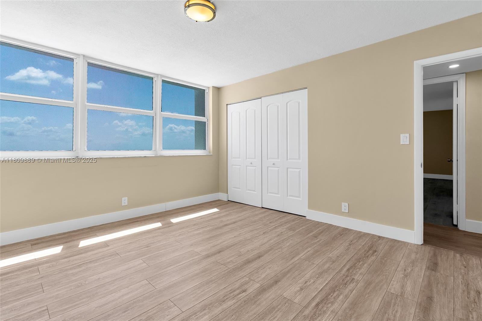 An empty room features light wood-look flooring, white closet doors, and large windows with sky views — 1904 S Ocean Dr # 1004, Hallandale Beach FL 33009, HALLANDALE BEACH, FL
