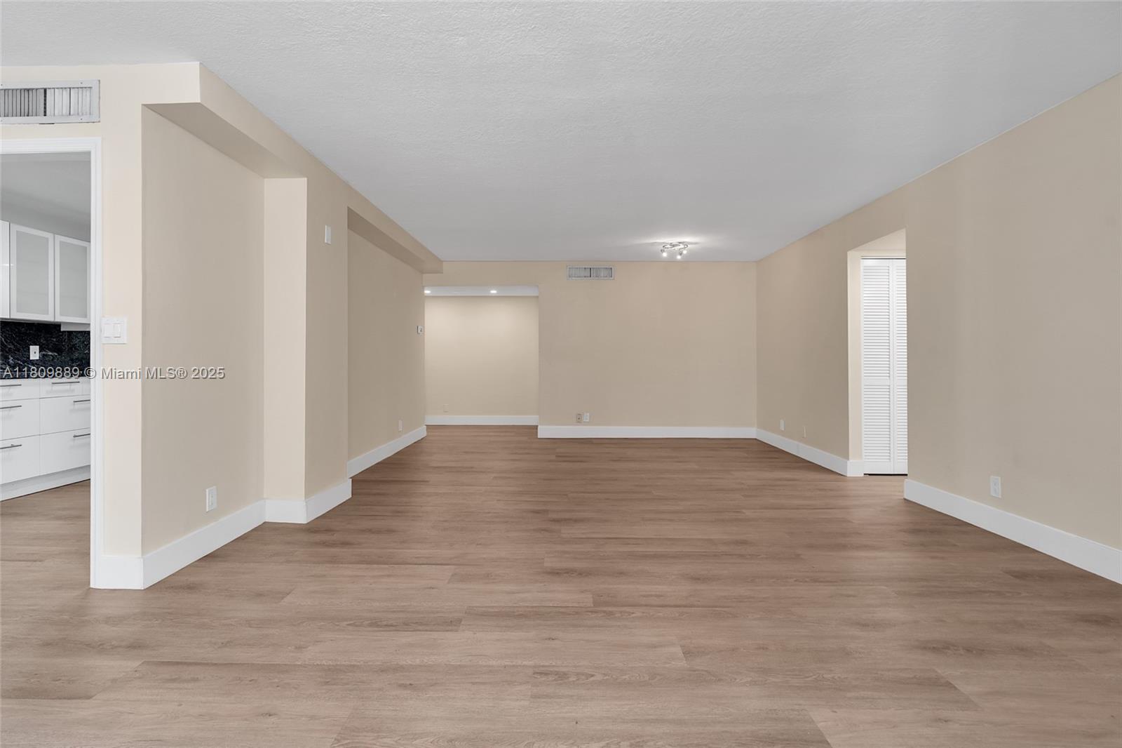 An empty room features light-colored walls, wood-look flooring, and a white kitchen visible to the left — 1904 S Ocean Dr # 1004, Hallandale Beach FL 33009, HALLANDALE BEACH, FL